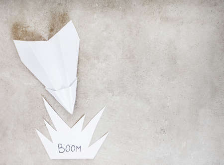 Paper airplane as metaphor, heading for a crash or explosion, on grey with copy spaceの写真素材