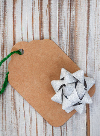 plain cardboard gift tag with green string and silver bow on rustic wooden surfaceの写真素材