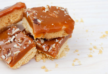 Pieces of shortbread topped with caramel and nuts on a wooden board. Selective focus.の写真素材