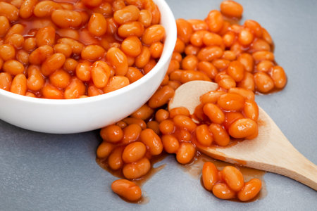 Baked beans in tomato sauce with wooden spoon on grey background.の写真素材