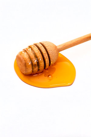 Honey dripping from a wooden honey dipper isolated on white backgroundの写真素材
