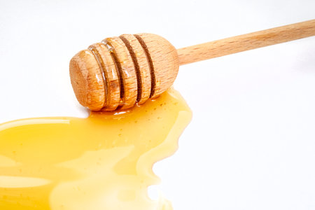 Honey dripping from a wooden honey dipper isolated on white backgroundの写真素材
