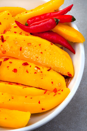 Slices of ripe mango with chili pepper in white bowl.の写真素材