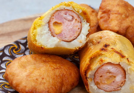 Traditional South African Russian sausage Sputnik or deep fried mash covered sausage on wooden board with traditional printed clothの写真素材