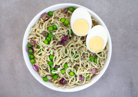 Instant noodles with green peas and boiled egg in white bowl, top viewの写真素材