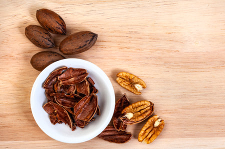 Pecan nuts with shell in white bowl on wooden background, top view. space for copy