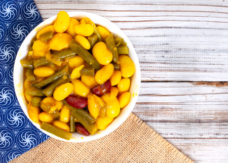 Flat lay of curried three bean salad in a bowl on table with iconic South African Shwe Shwe fabric on rustic woodの写真素材