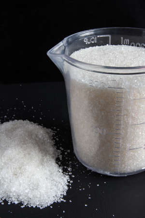 measuring cup with sugar on a dark backgroundの写真素材