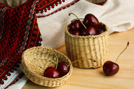 cherries in wicker bowl on a wooden table with a linen cloth in the background