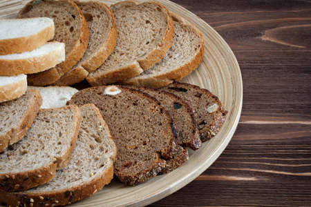 Different types of bread on a plate on a wooden table surface, top view