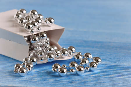 silver beads scattered in a paper bag on a wooden surfaceの写真素材
