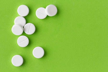 heap of white round medical pills on a bright green backgroundの写真素材