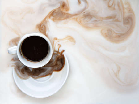 black coffee pouring from a white cup spread into milkの写真素材