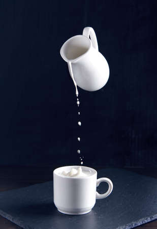 milk pouring from the milkman into a cup on a dark backgroundの写真素材