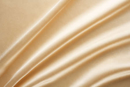 light shiny golden fabric draped with large folds, textile backgroundの写真素材