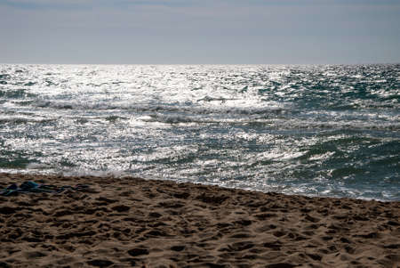 At the beach with rough sea with reflections from the sunの写真素材
