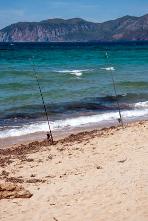 two fishing rods in the sea on the sand with mountains on the backgroundの写真素材