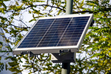 sustainable small solar panel with branches and leaves of trees in the background for the environmentの写真素材
