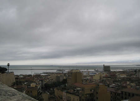 Cagliari's skyline with buildings, port, sea and gloomy grey cloudy sky in Sardiniaのeditorial素材