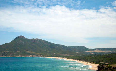 Landscape of Bugerru's coastline in Sardinia, with a cloudy blue sky, mountain, the beach and a rough sea for tourismの写真素材