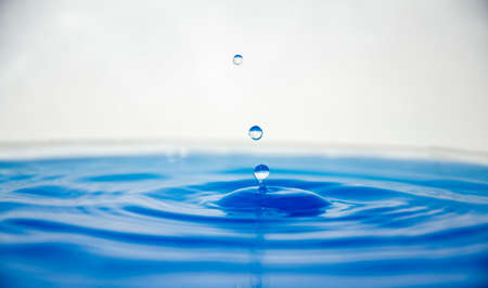 Drops of water falling on the water surface bluish with white backgroundの写真素材