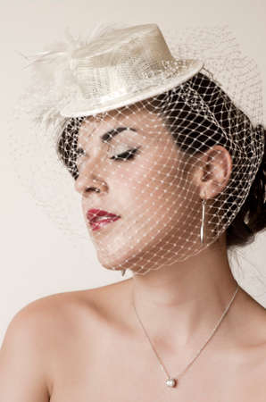 A portrait of a naked brunette girl with red lips, a necklace with shining stone as a pendant and a white hat with small fine net upon the face. It's meの写真素材
