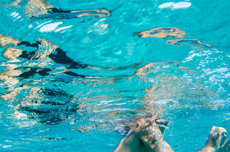 A male body underwater swimming in a clear blue mediterranean sea and the face out of the sceneの写真素材