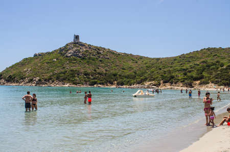 Porto Giunco, Italy - June 05: Unidentified people in beach Porto Giunco (Villasimius). Sunny day with people in the beach, transparent sea in summertime, and historical tower on the nountain behind on June 05.2015 in Villasimius, Italy as editorialのeditorial素材