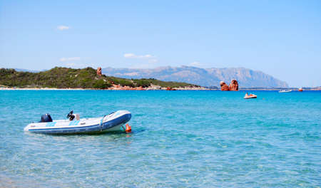 white rubber boat in the clear blue sea and mountains in the background for tourism in sardiniaの写真素材