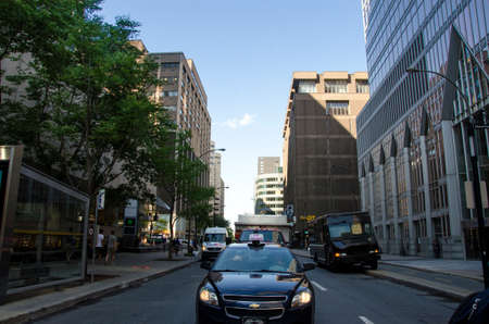 Montreal, Quebec, Canada - 18 July 2016 - Generic street and taxi in the front in downtown in Montreal in summertime. Cars, people and trees and buildings as editorialのeditorial素材