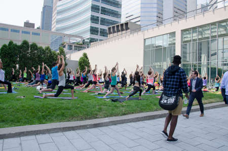 Montreal, Quebec, Canada - 20 July 2016 - A group of women practing yoga in a class in a green area in the center of the city with people walking on the sidewalk during summertime as editorialのeditorial素材