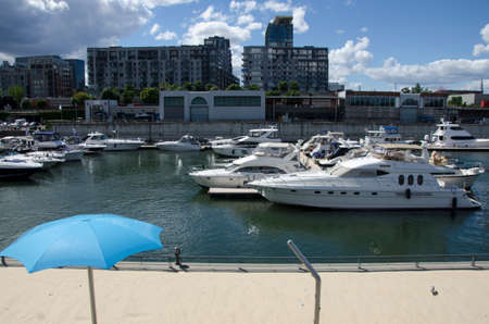 Montreal, Quebec, Canada- July 19 2016: White yachts in the port waiting during summertime. An artificial beach in the front and city/buildings in the background as editorialのeditorial素材