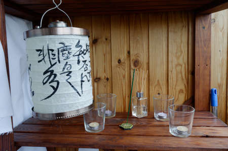 Composition in the Chinese style of four candles in glass candlesticks, aroma sticks and a Chinese lantern against a tree backgroundの写真素材