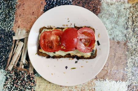 Rye bread sandwich with tomatoes, melted cheese, dark basil and chicken on a pink plate