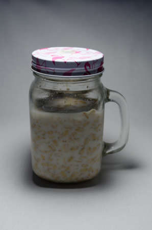 Oatmeal with milk in a transparent jar with pink with a white lid on a white rag backgroundの写真素材
