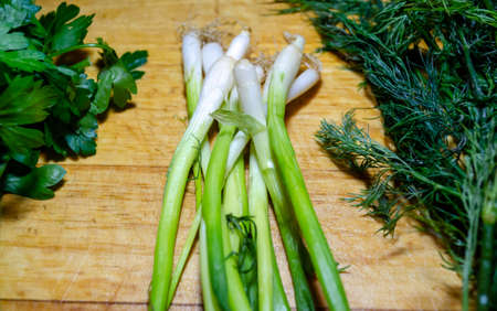 Sheaves of green onions, parsley and dill on a wooden cutting board top view