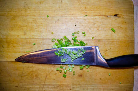 Finely cut green onions on a kitchen metal shiny knife on a wooden board for cutting vegetables in...