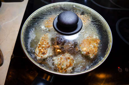 fried chicken mince patties with green on the blue iron pan under transparent glass cover top view