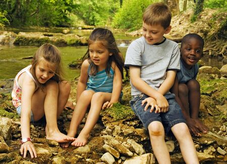 Four small children on rocks in the water.の写真素材