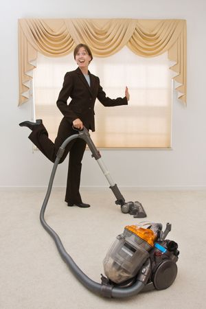 Young woman in a  suit vacuuming in an exaggerated pose. Selective focus on the vacuum.の写真素材
