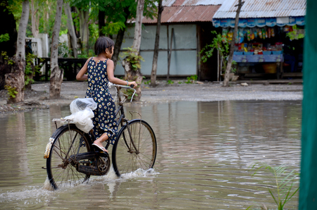 Burmese girl riding bicycle in flood area after raining at village between go to Mandalay Palace on May 19. 2015 in Mandalay, Myanmar.のeditorial素材