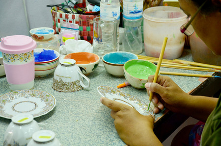 Thai people woking process paint Ceramic Benjarong is traditional thai five basic colors style pottery at workshop of Ban Don Kai Dee (Benjarong Village) on August 8, 2015 in Samut Sakhon Thailand.のeditorial素材