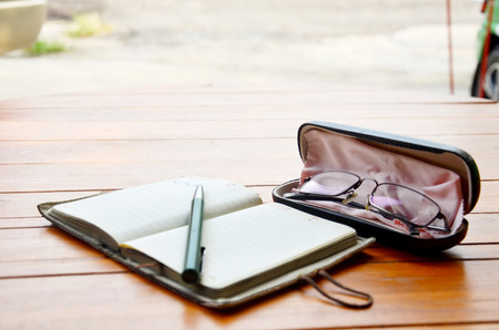 Pen on note book and Spectacles glasses on wooden tableの写真素材