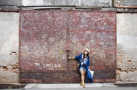 Thai woman travel and portrait with dirty Iron steel red door old classic style at George Town and street art area on April 27, 2016 in Penang, Malaysia.の写真素材
