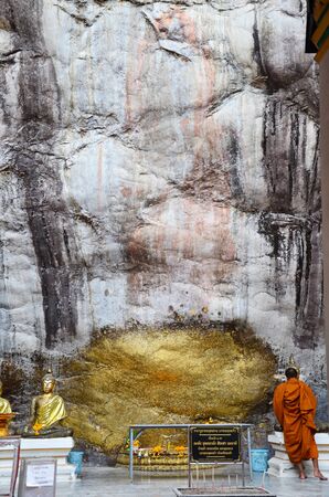 Monk respect praying and gild cover with gold leaf at Lord Buddha image appearing on a cave and cliff wall at Wat Phra Phutthachai on July 28, 2015 in Saraburi, Thailandのeditorial素材