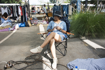 Thai women sitting and playing mobile phone while waiting customer in clothes shop at street market fair on November 26, 2017 in Nakhon Ratchasima, Thailandのeditorial素材