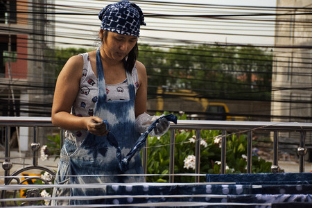 Thai women working Indigenous knowledge of thailand tie batik dyeing indigo color or mauhom color and hanging process dry fabric in the sun at outdoor on top of house in Nonthaburi, Thailandの写真素材