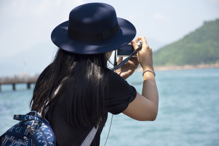 Travelers thai woman sitting relax and take photo with view landscape of island and sea at Victoria Harbour near Shing Sai road at Kennedy Town in Hong Kong, Chinaの写真素材