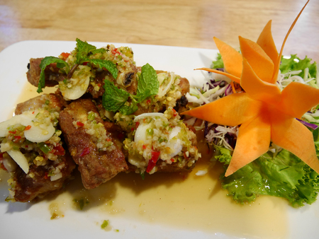 Fried pork spare ribs with garlic and pepper mix with spicy salad in plate on table at restaurant in Nonthaburi, Thailandの写真素材