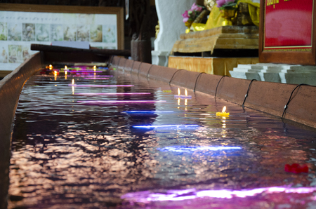 Ritual praying colorful candle floating on water for pray reclining Buddha image at Wat Phra Non Chakkrasi Worawihan temple at Singburi city in Sing Buri, Thailand.の写真素材